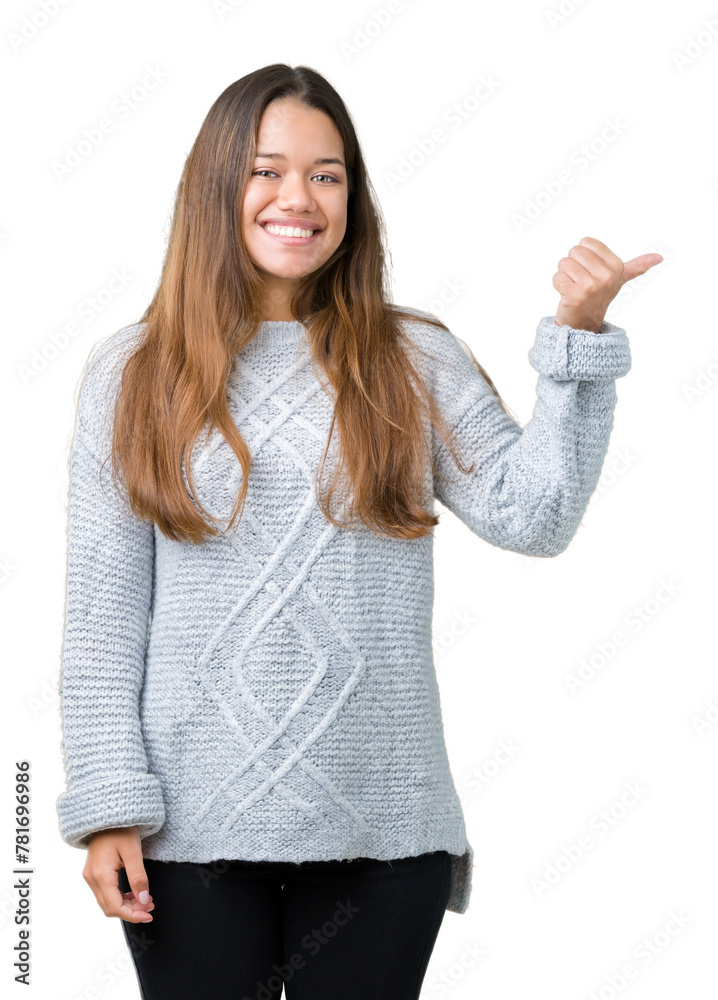 Young beautiful brunette woman wearing sweater over isolated background smiling with happy face looking and pointing to the side with thumb up. Young beautiful brunette woman wearing sweater over isolated background smiling with happy face looking and pointing to the side with thumb up.