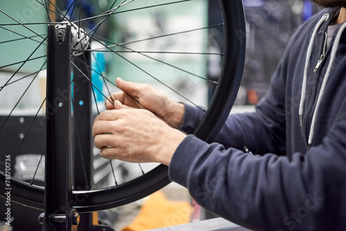 Unrecognizable man checking the tension of the spokes of a bicycle wheel in his bike workshop. Real people at work.