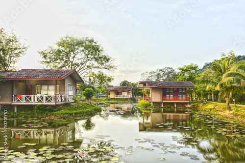 Baan Rim Nam. Beautiful landscape view of three house wooden with reflect shadow on water pond isolated with green nature background. Home traditional design for create to help cool down in summer.