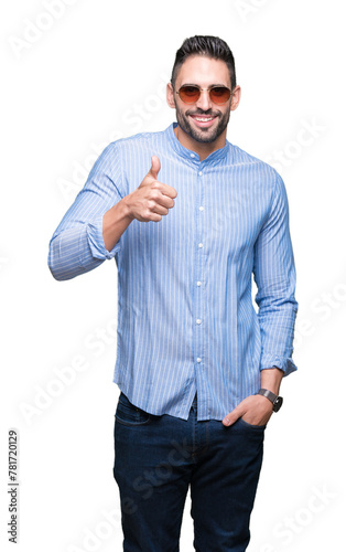 Young handsome man wearing sunglasses over isolated background doing happy thumbs up gesture with hand. Approving expression looking at the camera with showing success. © Krakenimages.com