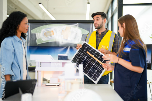 Focused construction specialists evaluate a solar energy panel model in a modern workspace with design drafts.