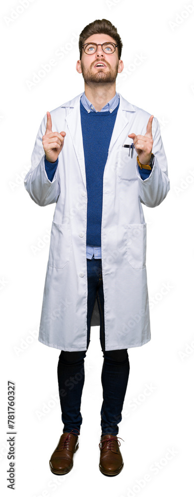 Young handsome scientist man wearing glasses amazed and surprised looking up and pointing with fingers and raised arms. Young handsome scientist man wearing glasses amazed and surprised looking up and pointing with fingers and raised arms.