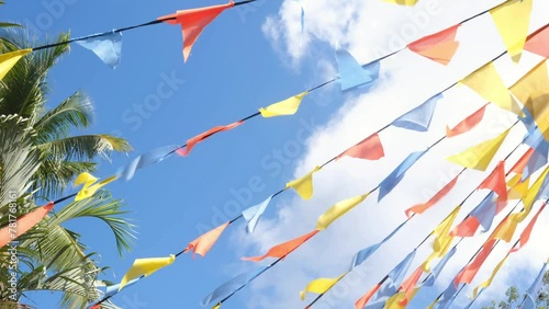 Colorful triangle bunting flags or banderitas hanging and blown by wind against blue sky. Celebration and fiesta concept. photo