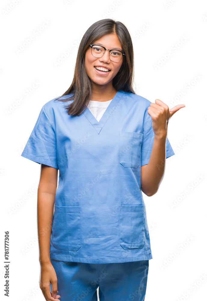 Young asian doctor woman over isolated background smiling with happy face looking and pointing to the side with thumb up. Young asian doctor woman over isolated background smiling with happy face looking and pointing to the side with thumb up.