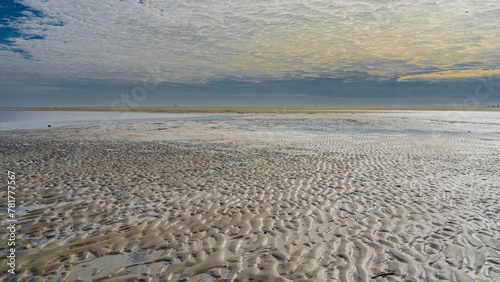 The low tide in the ocean. The wavy pattern of the sandy ridges of the exposed seabed. Puddles of water on the sand. Picturesque clouds in the blue sky. The boundless expanse. Madagascar. Morondava. 