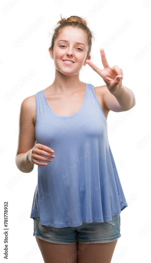 Young blonde woman smiling looking to the camera showing fingers doing victory sign. Number two.