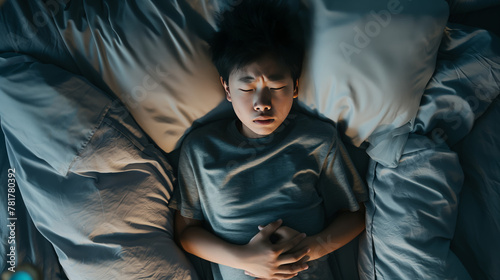 An overhead shot of a young boy feeling unwell in bed, his expression and pose suggest discomfort or illness photo