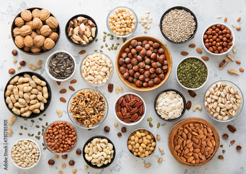 Mixed assorted raw healthy nuts and seeds in various bowls on light kitchen background.Peanut,hazelnut,walnut,almonds,pistachio,sunflower,pumpkin,chia and cashew.Top view. © DenisMArt