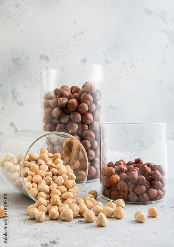 Glass jars with healthy raw hazelnut whole and peeled nuts on white kitchen table.Macro.