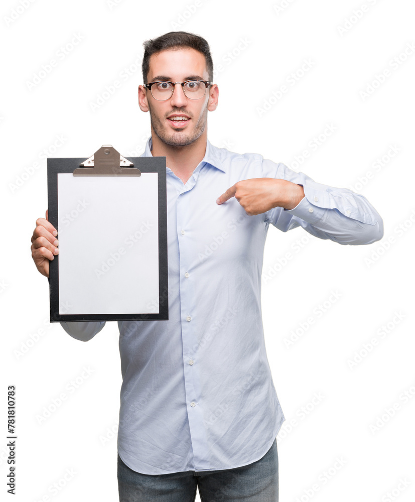 Handsome young business man showing a clipboard with surprise face pointing finger to himself Handsome young business man showing a clipboard with surprise face pointing finger to himself