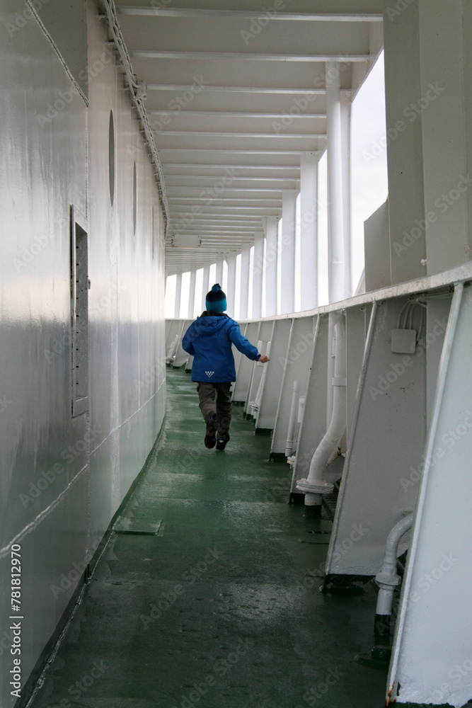 Ein Kind rennt auf dem Gang an Deck eines Schiffes davon Ein Kind rennt auf dem Gang an Deck eines Schiffes davon