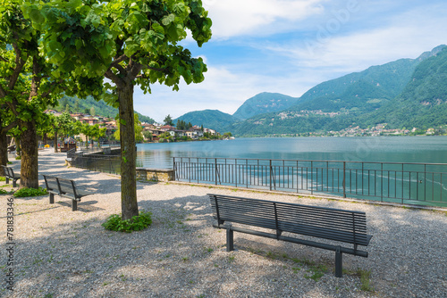 Park with benches on the shore of a lake surrounded by mountains. Lake Lugano and the town of Riva San Vitale, Switzerland, at the foot of Monte San Giorgio UNESCO site for fossiliferous deposits