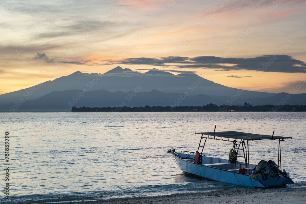 Tourist boat in  at the shore of tropical Gili Meno island overlooking Lombok island and Rinjani volcano in  Indonesia at sunrise