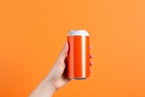 Female hand holds a can of soda on an orange background. Copy space.