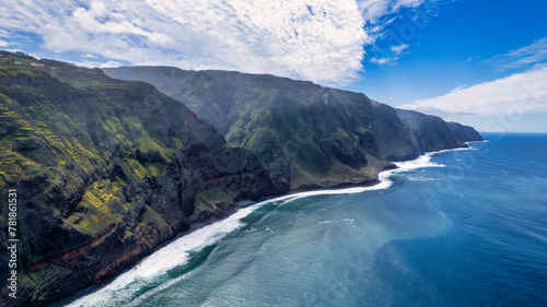 Fototapeta Naklejka Na Ścianę i Meble -  The coast of Madeira; green, rocky cliffs border with the white, frothy waves of the ocean, showcasing the contrast of natural elements.