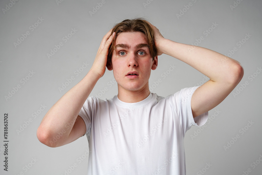 Young Man With Shocked Expression Holding Head Against a Gray Background Young Man With Shocked Expression Holding Head Against a Gray Background