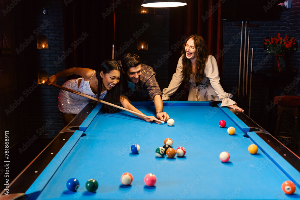 Fototapeta premium Young diversity group of people playing pool together with smile, enjoyment and fun. Young people spend time in billiards room at the nightclub. Men, women friends playing billiards. Nightlife concept