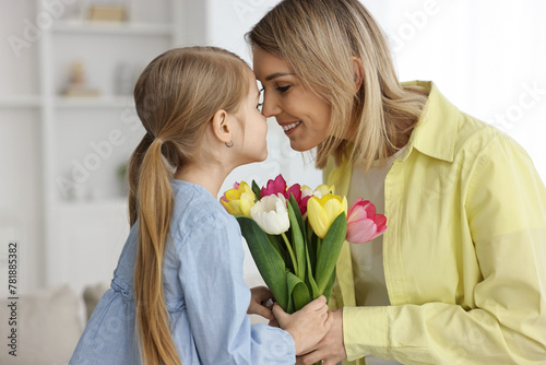 Little daughter congratulating her mom with bouquet of tulips at home. Happy Mother's Day