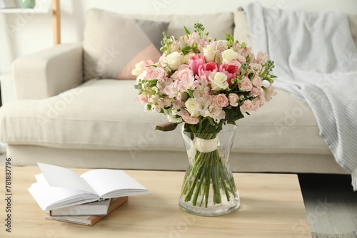 Beautiful bouquet of fresh flowers in vase and books on wooden table indoors © New Africa
