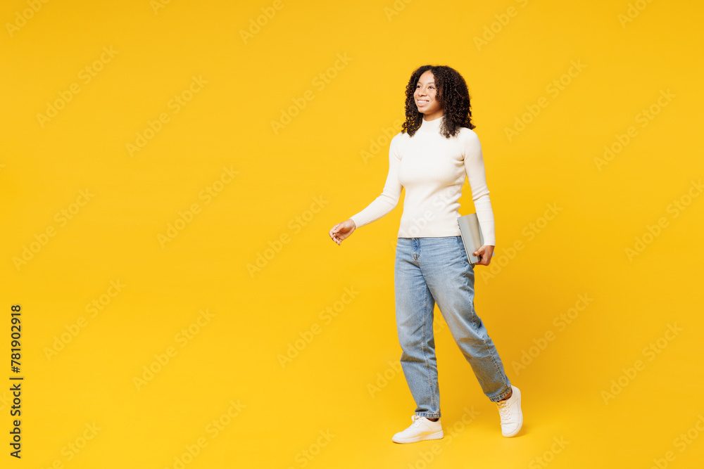Full body smiling fun little IT kid teen girl of African American ethnicity wear white casual clothes hold laptop pc computer go isolated on plain yellow background studio Childhood lifestyle concept Full body smiling fun little IT kid teen girl of African American ethnicity wear white casual clothes hold laptop pc computer go isolated on plain yellow background studio Childhood lifestyle concept