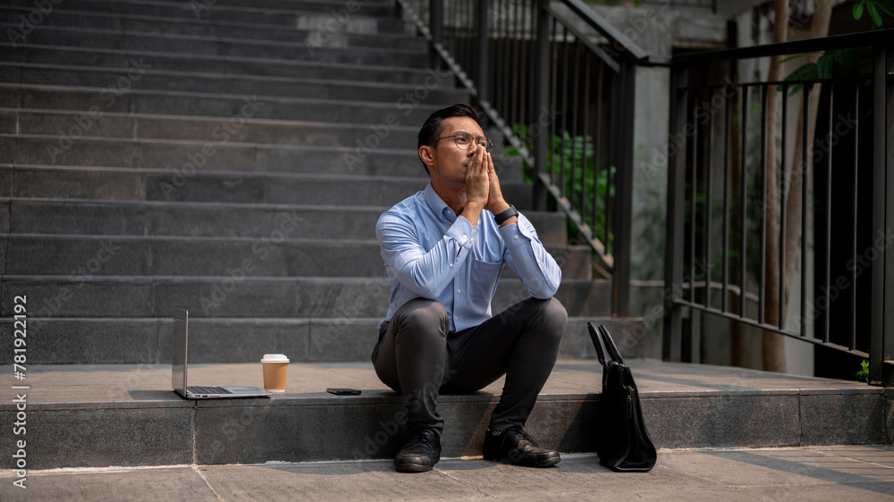 An Asian businessman sits on outdoor steps, experiencing frustration and the fear of being fired. An Asian businessman sits on outdoor steps, experiencing frustration and the fear of being fired.