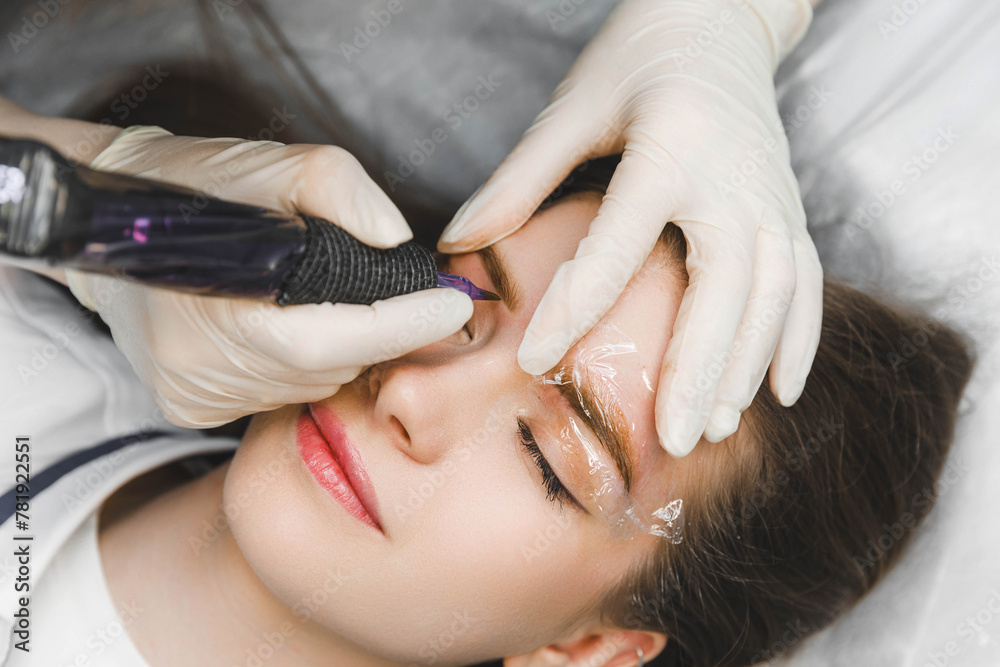Fototapeta premium A cosmetologist applies permanent makeup to the eyebrows - eyebrow tattoo. eyebrow perm