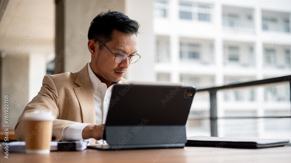 © bongkarn - A focused Asian businessman is working on his digital tablet and reviewing business document.