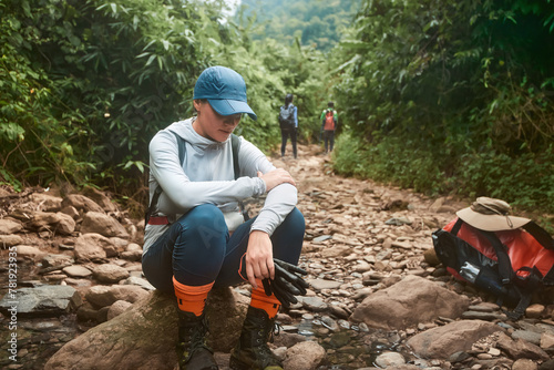 Tired woman hikker resting while trekking with group in wild jungle photo