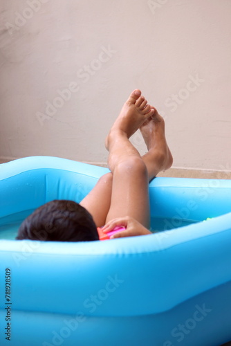 Cute little 3 year old boy is sitting in a sea blue bath tub.child is enjoying summer with water and chilling with his own thoughts and  relaxing. best summer outdoor activity for fresh air. 