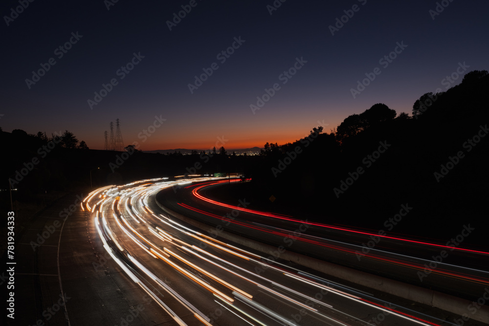 View of light streaks created by traffic coming from San Francisco and Oakland at sunset, as seen from an overpass over Highway 24.