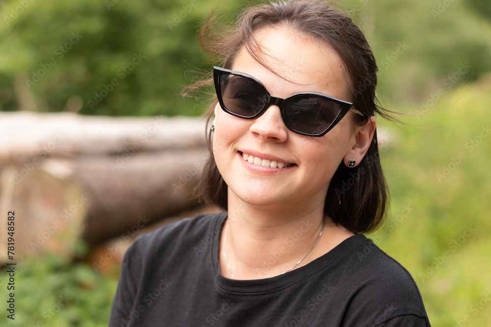 Front view of a beautiful girl in sunglasses on a blurred natural background and cut tree trunks