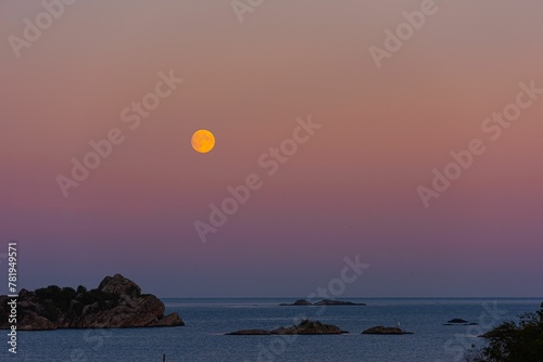 Full moon rising over the ocean in a pinkish and cloudless sky