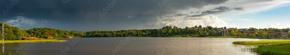 Panoramic view of lake surrounded by green field under cloudy sky