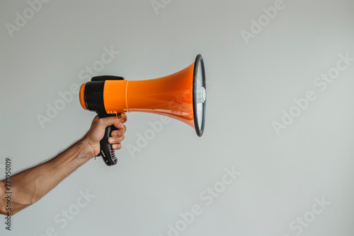 Strong Arm Holding Orange Megaphone Against a Neutral Background photo