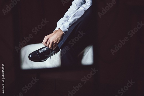 Man sitting on the bed and lacing up his leather shoes on his wedding day