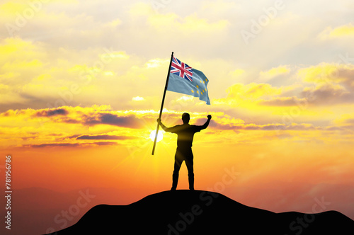 Tuvalu flag being waved by a man celebrating success at the top of a mountain against sunset or sunrise. Tuvalu flag for Independence Day.