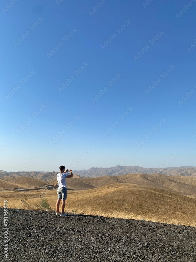 Vertical shot of a man standing and photographing the hills on a sunny day