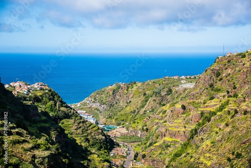 Aerial shot of the landscape with buildings between hills and a seascape in the background