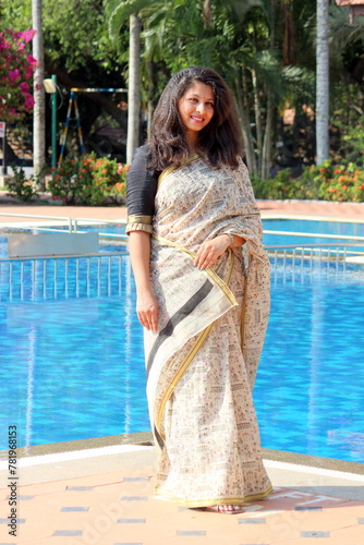 a woman at south india in black and white saari drapped in bengoli style. Lady is standing in front of a nice swimming pool at a resort. she is wearing light makeup and crimped hair for festive look. photo