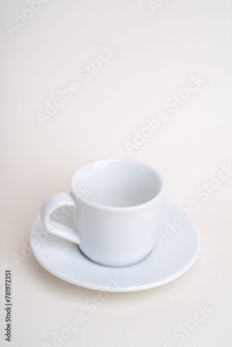 Vertical shot of a white cup of coffee with its plate on a cream surface