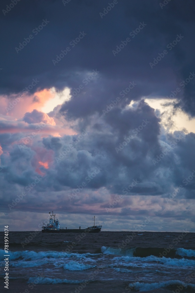 Vertical shot of an industrial ship sailing on water at sunset