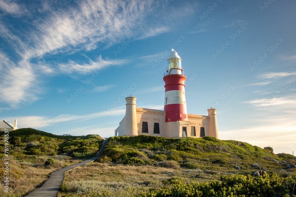 Image of a white and red lighthouse on the top of the mount under the blue sky.