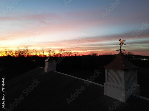 Horse weathervane on the cupola and the silhouette of trees against the orange-red sky at the sunset