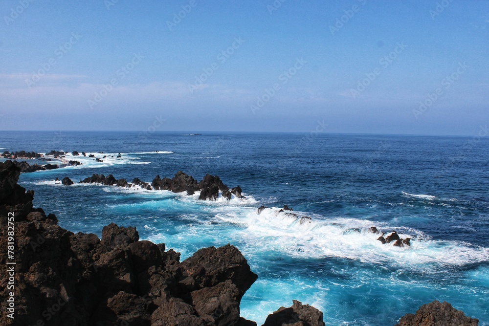 Seascape blue sea and white foamy waves beside brown rocks