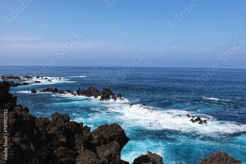 Seascape blue sea and white foamy waves beside brown rocks © Wirestock