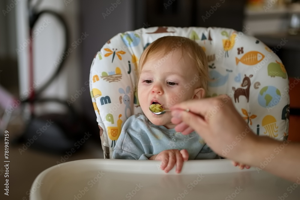 Baby girl sitting in high chair while her father feeding her Baby girl sitting in high chair while her father feeding her