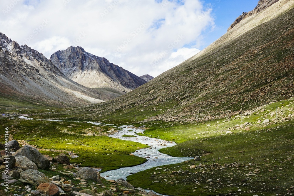 Scenic view of a meadow with a frozen river and rocky hills in the background under sunlight