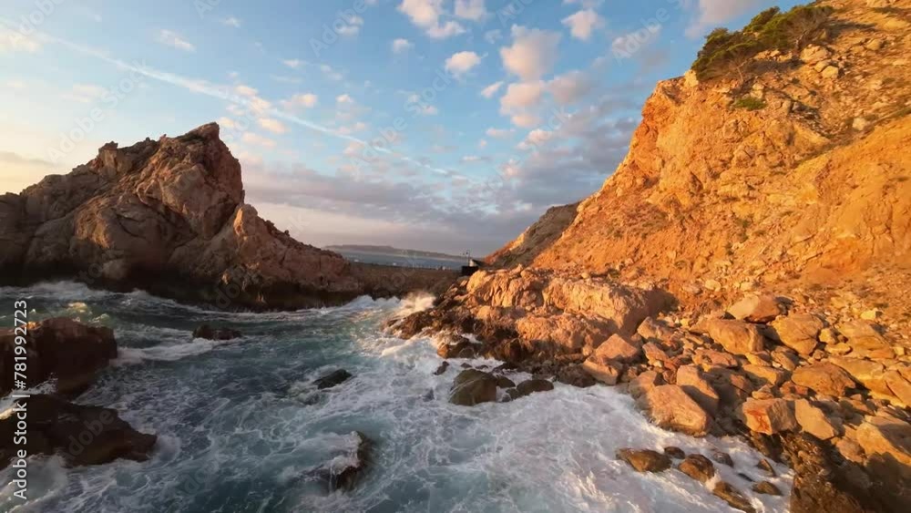 Drone shot of foamy strong waves hitting the rocks of rugged cliffs at the sea coast under sunshine Drone shot of foamy strong waves hitting the rocks of rugged cliffs at the sea coast under sunshine