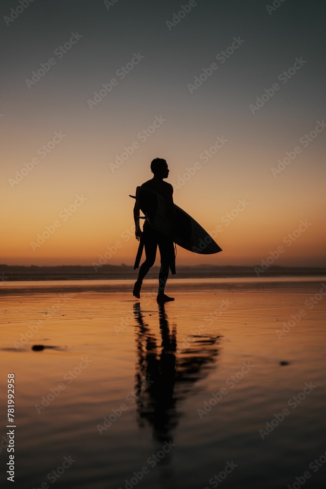 Vertical shot of a person with a surfing board walking on the beach at sunset perfect for wallpapers