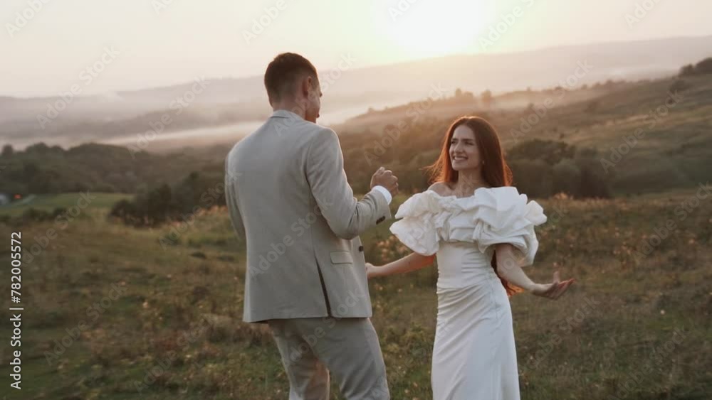 The bride and groom walk at sunset through beautiful fields and hills, laugh and dance. Wedding day concept The bride and groom walk at sunset through beautiful fields and hills, laugh and dance. Wedding day concept